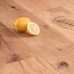 Eine ganze und eine halbe Zitrone liegen zusammen auf einem Holzboden. Der Boden hebt sich durch seine natürliche Maserung hervor.